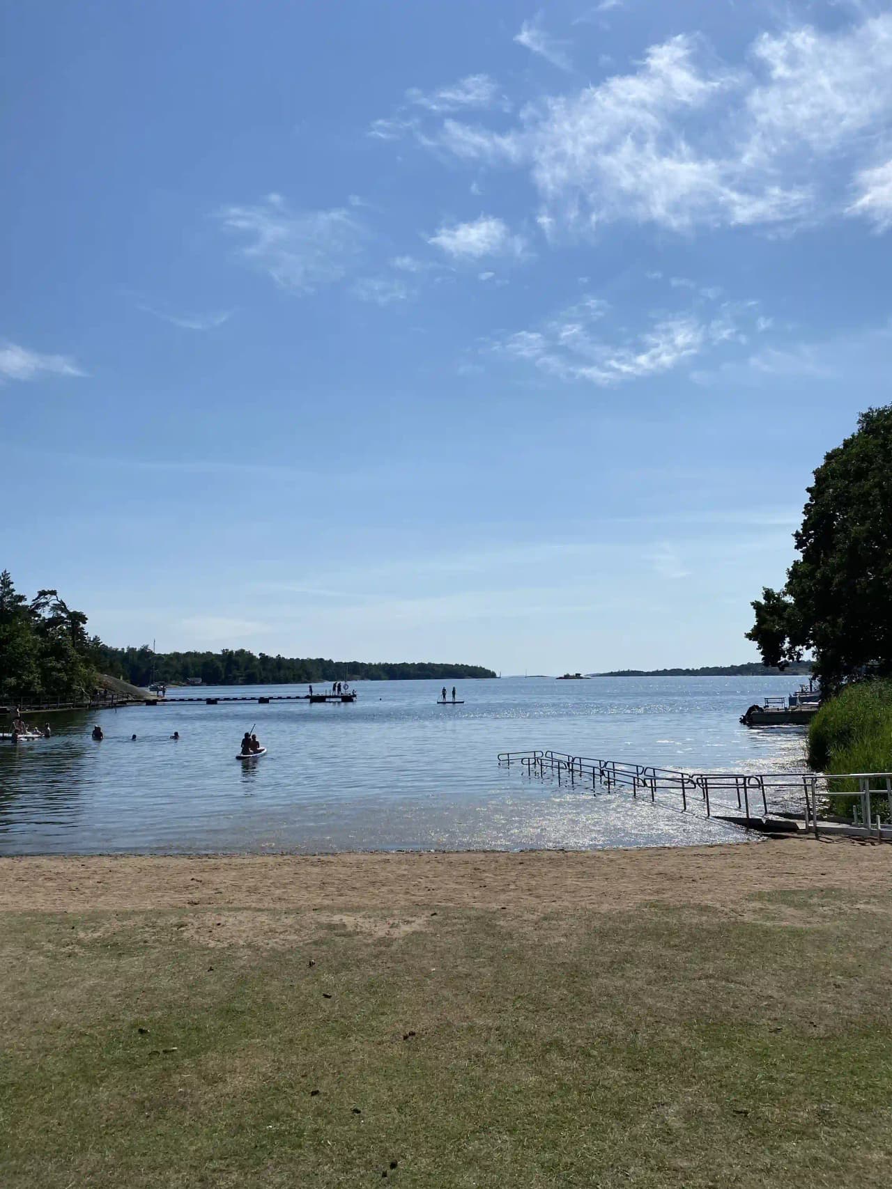 En solig sommardag vid vattnet på Järnaviks camping, med en kustlinje som sträcker sig mot horisonten och mjuka moln svävande över den klara himlen.