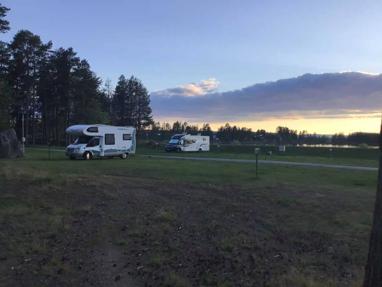 En husvagn står parkerad på en grön gräsyta under en delvis molnig himmel vid Storuman Campingen.