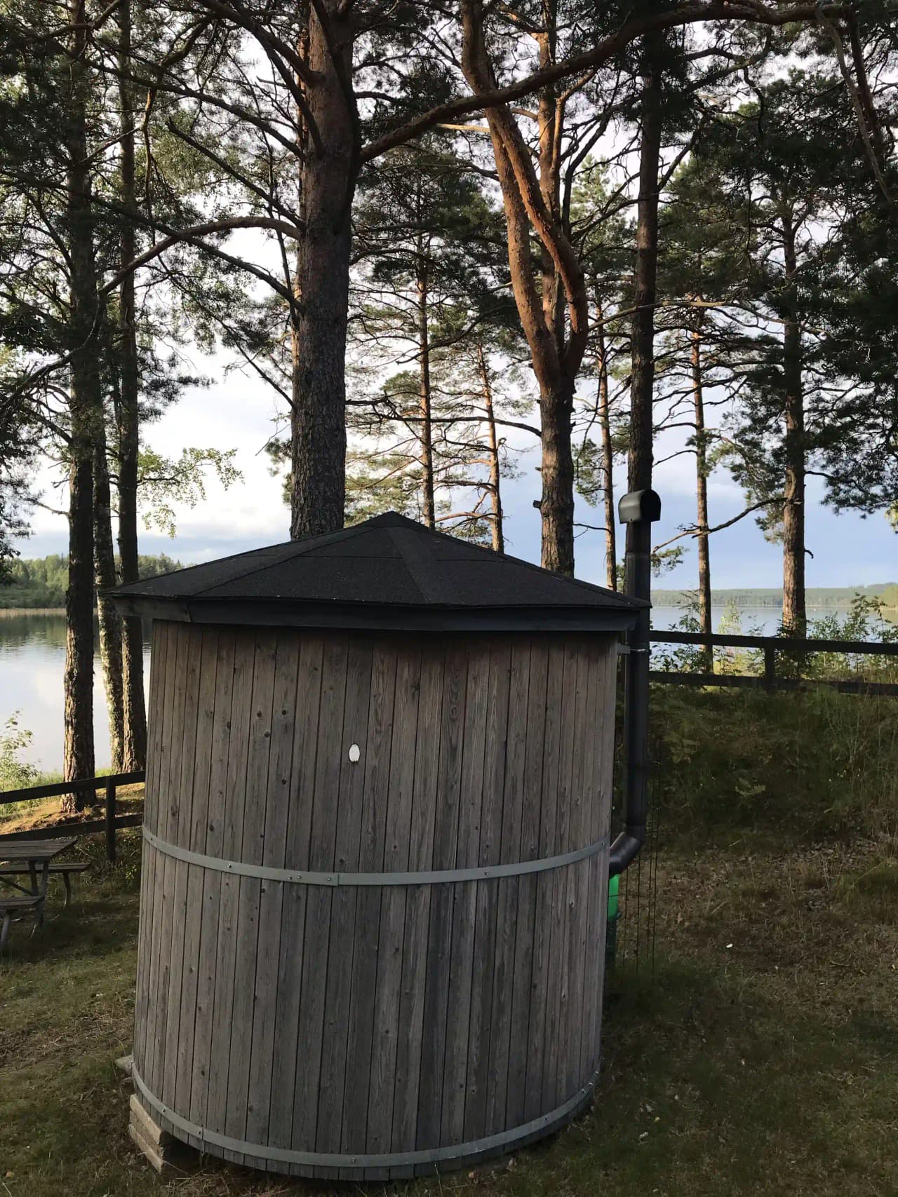 En trästuga placerad vid Horndals Bad & Camping, omgiven av grönskande natur och en välskött gård. Byggnaden har en enkel, rustik stil med plankor och synligt träverk, vilket ger en charmig och inbjudande atmosfär i en avkopplande miljö.