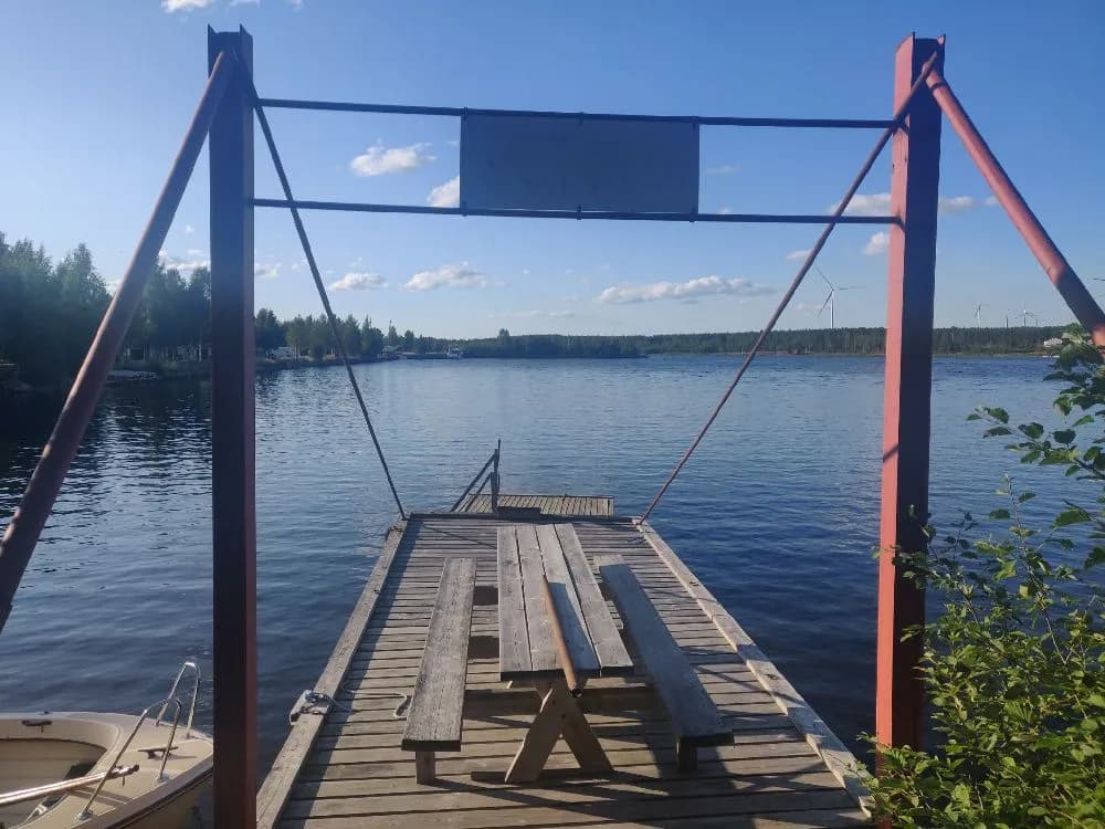 En trädocka sträcker sig ut över en lugn sjö vid kvällstid på Sikeå Havscamping, omgiven av trä och naturskön miljö.