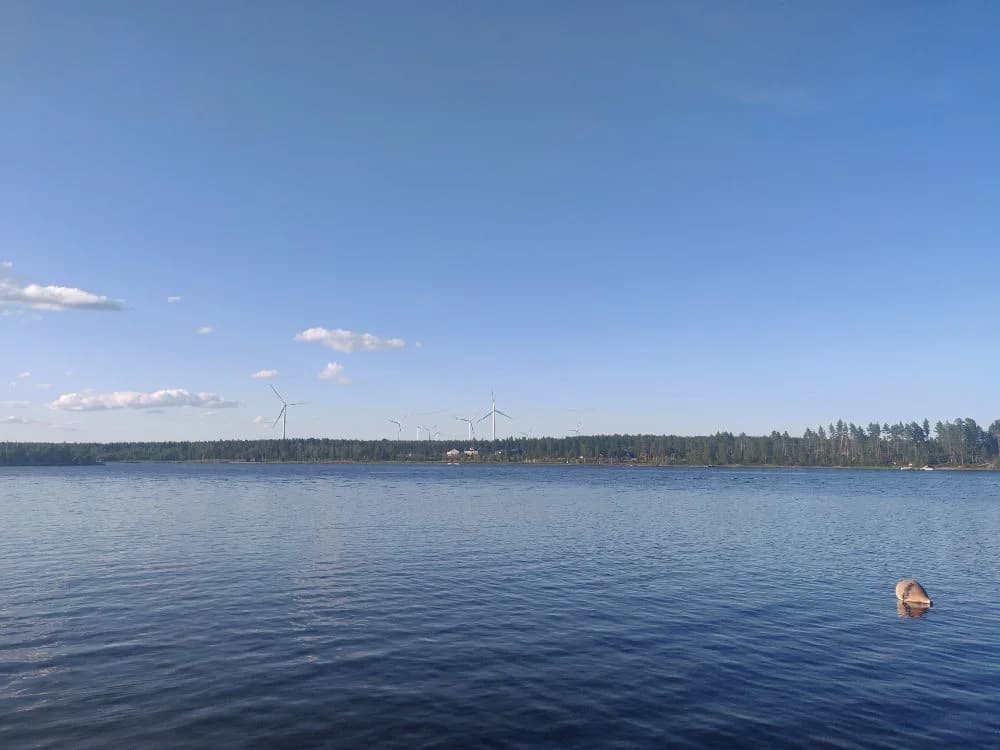 Vy över Sikeå havscamping med blå himmel och klarblått vatten i förgrunden. Horizontlinjen syns tydligt, vilket skapar en lugn och vidsträckt känsla av natur och vidd.