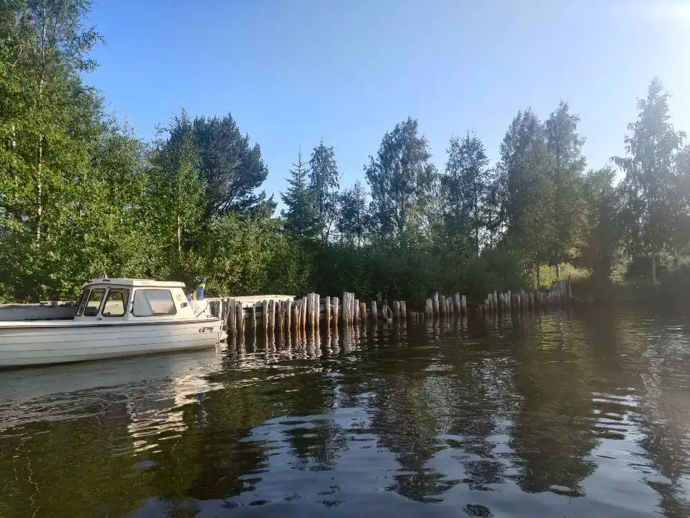 Bild av Sikeå Havscamping med en vattenväg där flera båtar är förtöjda. Vattnets yta reflekterar den omgivande naturen. 