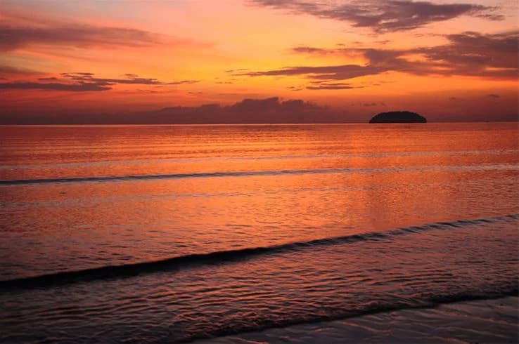 En solnedgång vid Askeviks camping & stugor med orange himmel och moln horisontellt över ett stilla vatten.