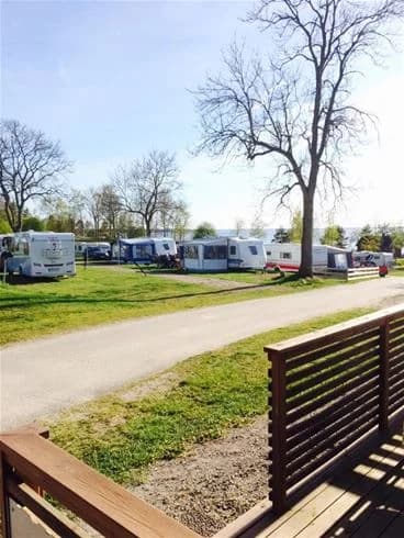 En campingplats med parkerade husvagnar och husbilar, omgiven av ett staket. En asfalterad gångväg leder genom området som har ett öppet och naturnära utseende.