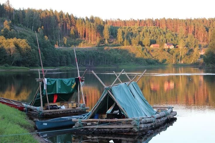Vy över Björkebo Camping vid en sjö med flera båtar vid vattenbrynet, omgivna av grönska och en stilla vattenyta.
