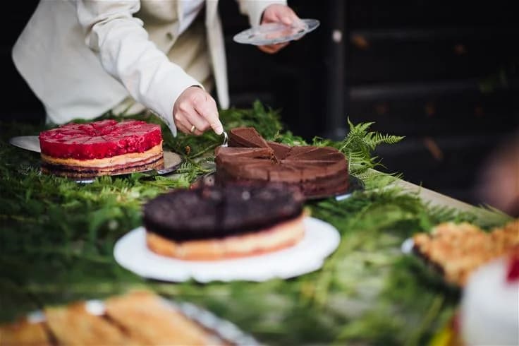 En dekorerad tårta med färgglad glasyr och strössel, placerad på ett bord utomhus vid Björkebo Camping. Tårtan är en del av en picknick eller firande, inramad av naturskön miljö.