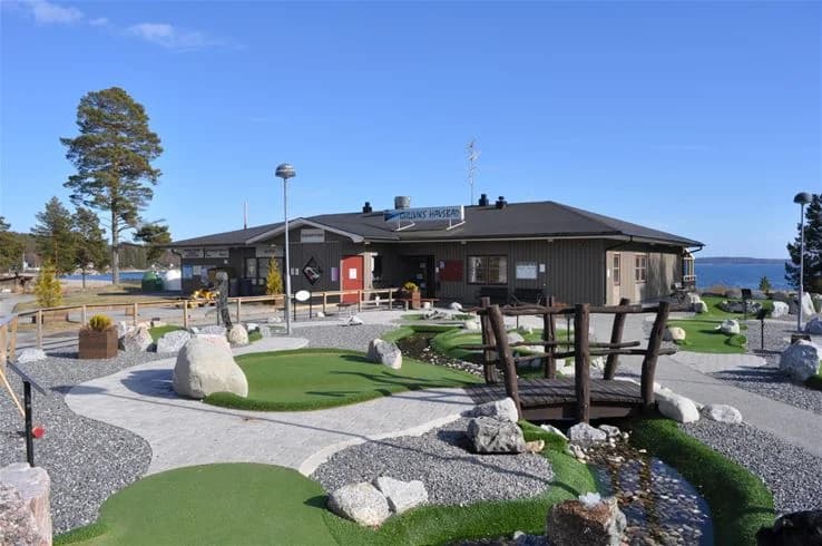 Bilden visar ett öppet campingområde med stugor och gröna områden. Det finns träd och buskage som ger skugga samt uppfarter som leder till olika delar av campingen. Området ser välskött och inbjudande ut, perfekt för utomhusaktiviteter och avkoppling.