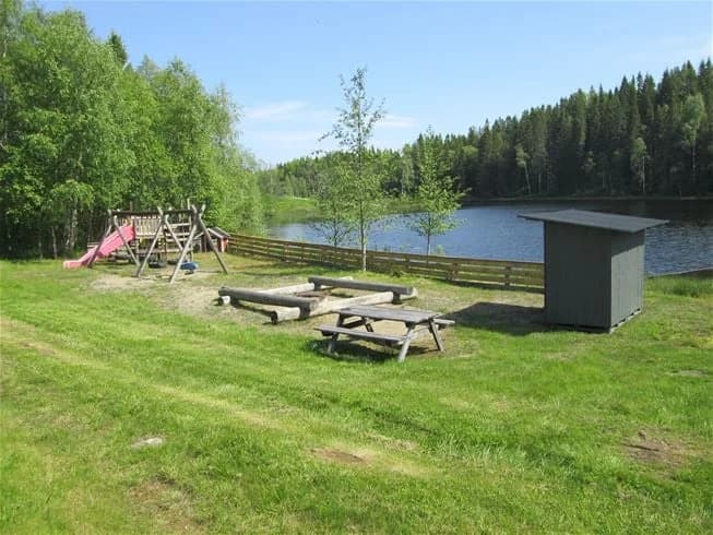 Bild av Antjärns camping där ett vattendrag slingrar sig genom den naturliga miljön, omgiven av lummig grönska. På stranden av sjön finns en utemöbel som ger en plats att koppla av och njuta av naturen.