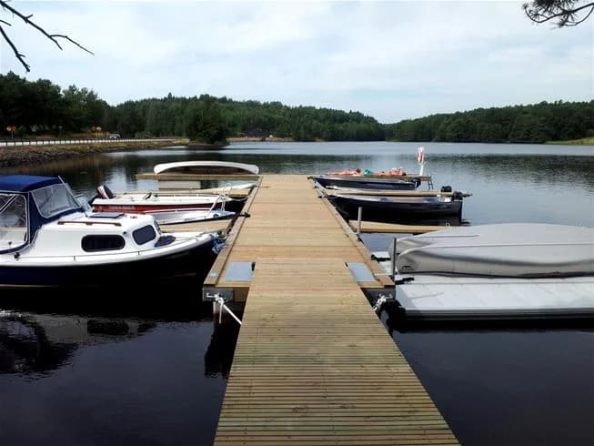 En båt ligger förtöjd vid en brygga vid Långsjön, omgiven av stilla vatten och skog i bakgrunden.