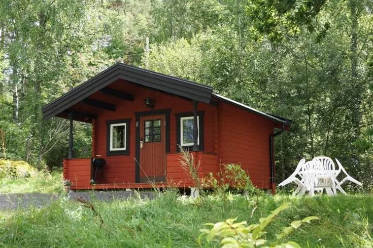 En trästuga med tak i en lantlig miljö, omgiven av träd och grönska.