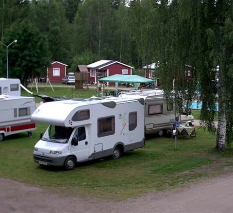 En husvagn och husbil parkerade på en grön gräsmatta vid Camping 45, med träd i bakgrunden.