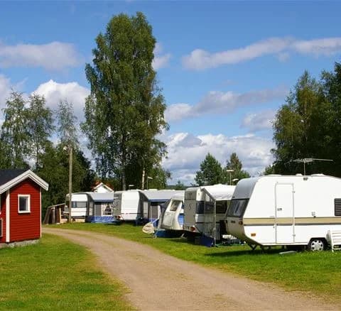 En grön campingplats med gräsmatta och flera husvagnar samt husbilar parkerade. Området omges av frodiga växter och terrängen är plan och välskött.