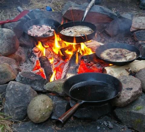 En lägereld med kokkärl och matlagning över glödande kol på Camping 45.