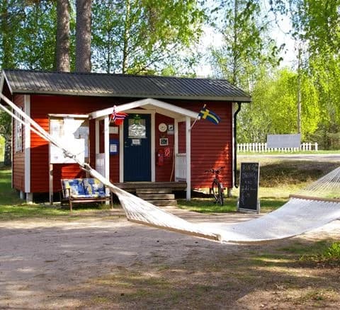 En trästuga omgiven av en välskött gräsmatta och inbäddad i en skuggig, lummig miljö på camping 45.