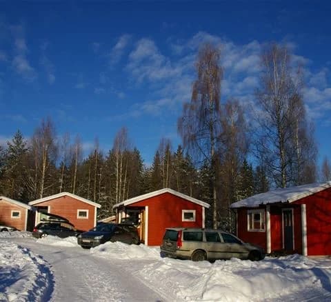 En snötäckt stuga omgiven av träd i ett vinterlandskap på camping 45.