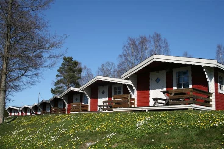 En stuga omgiven av en grön gräsmatta och träd, med trädgårdsbyggnader och trädgårdsmöbler i närheten vid Sikhalls Camping.