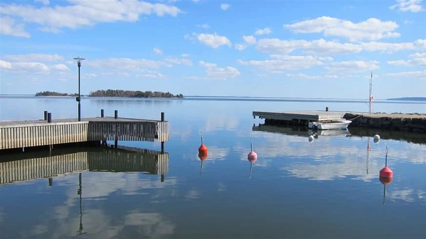 En brygga sträcker sig ut över ett spegelblankt blått vatten vid Sikhalls camping, omgiven av en vidsträckt horisont och en lugn sjö.
