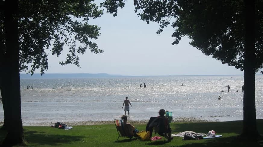 En solig sommardag vid Sikhalls camping med vy över en kustlinje där stranden möter ett glittrande vattendrag. Perfekt för rekreation och avkoppling.