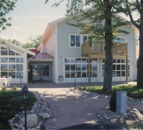 Bild av Villa Björkhagen, ett hus med gräsmatta och uppfart i förgrunden. Huset har en dörr, sidopaneler och är omgiven av landskapsarkitektur och skuggade delar av gården.