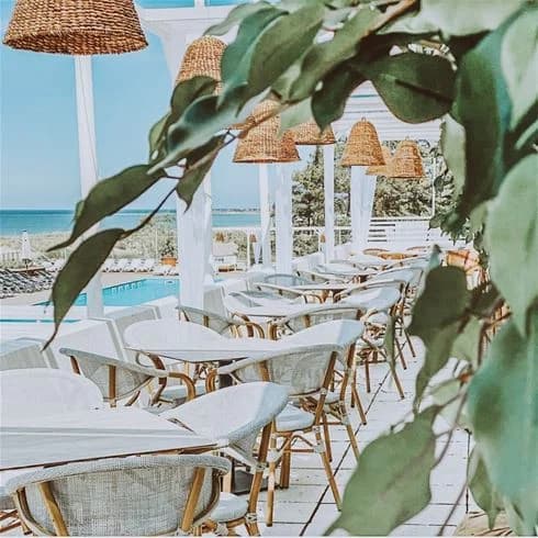 Bild av en uteservering vid Tofta Camping, med utomhusmöbler inklusive stolar och bord under parasoller, belägen nära stranden och omgiven av en semesterorts atmosfär.