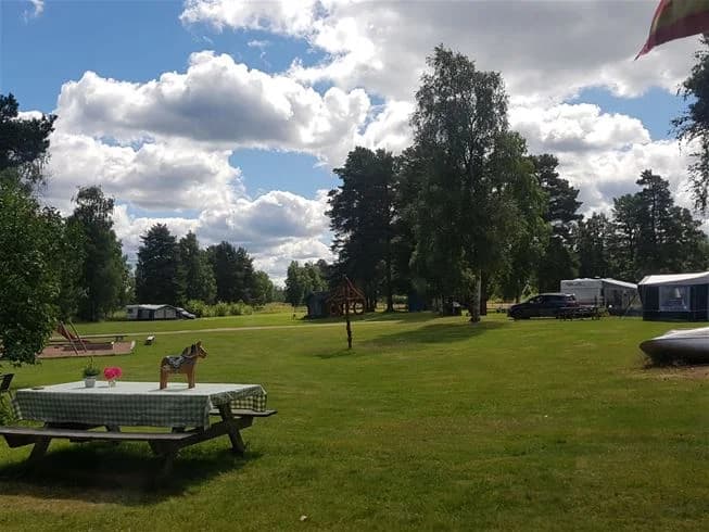 Vy över en öppen gräsplan omgiven av träd och molnig himmel vid Nås camping, en plats för rekreation och utomhusaktiviteter.