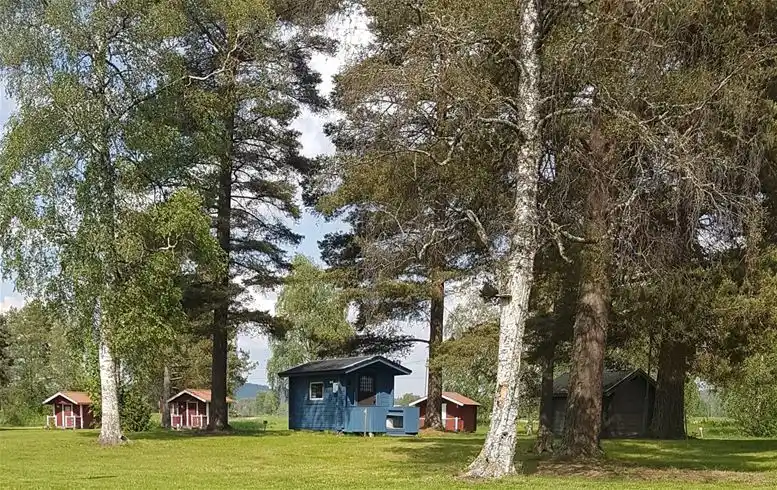 En grönskande campingplats vid Nås med gräsfält, träd och ett pittoreskt stugområde i ett lantligt landskap.