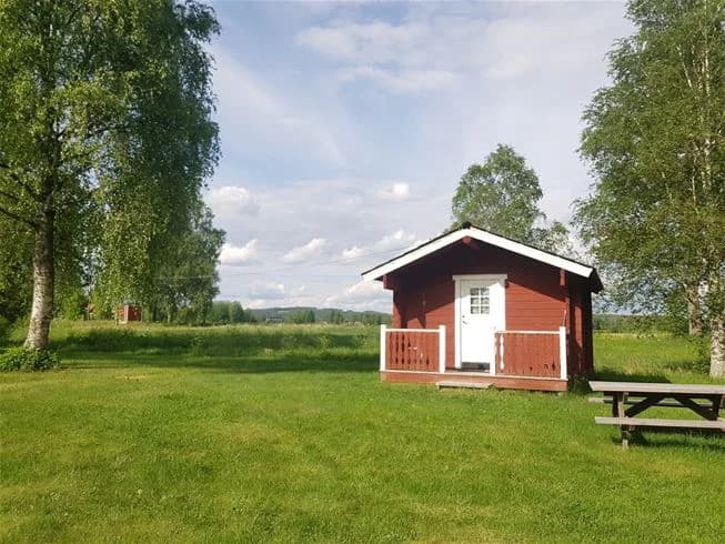 En grön gräsplan med ett hus och en stuga i ett lantligt område, troligtvis en campingplats.