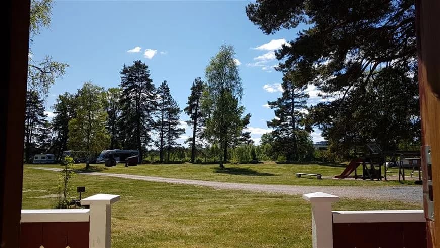 En grönskande campingplats med gräsbevuxna ytor och små stugor omgivna av träd och buskage, vilket ger en inbjudande och avkopplande miljö.