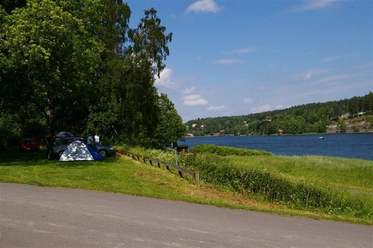 Bild på Grännäs Camping och Stugby: En naturskön plats vid vattnet med gröna gräsmattor och en båt vid strandkanten, omgiven av sjö och kustlandskap.