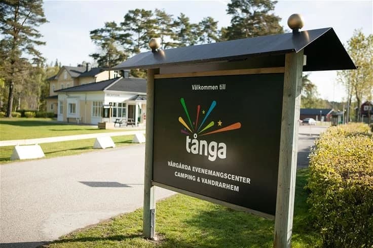 En campingplats med flera tält uppställda i skuggan av träd och stolpar.