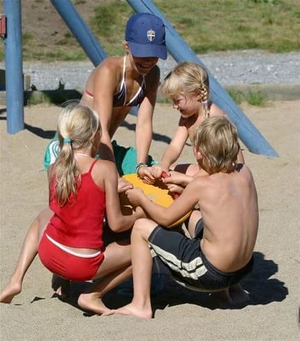 Barn som leker i sanden på Skellefteå camping en solig sommardag, med kortbyxor och hatt i en avslappnad semesteratmosfär.