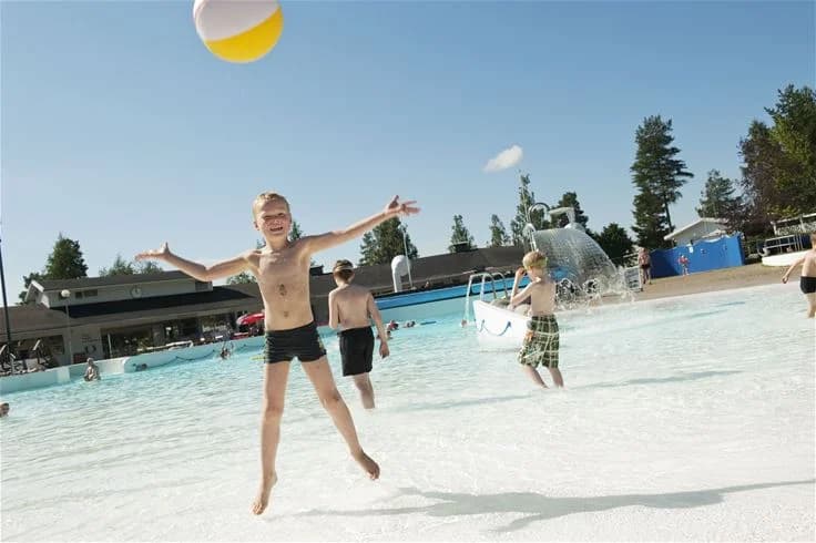 En familjevänlig campingplats i Skellefteå med en livlig semesteratmosfär. Gäster njuter av fritidsaktiviteter vid swimmingpoolen, många i baddräkter, som för tankarna till ledig semester och avslappning.