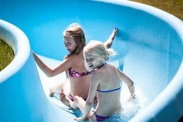 En glad blond flicka i baddräkt leker i en vattenpark på Skellefteå Camping under sommaren. Hon ser ut att ha roligt och njuter av sin semester.