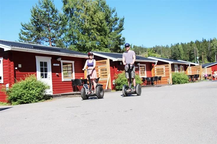 En campingplats i Skellefteå med grönskande gräsmattor, picknickbord och bänkar. Det finns parkeringsutrymmen och cyklar står parkerade i närheten, vilket skapar en inbjudande miljö för friluftsaktiviteter och avkoppling.