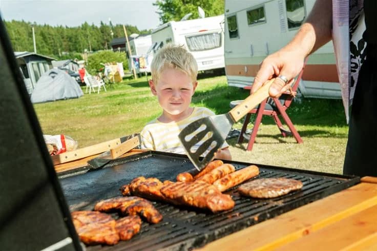 En bild på en utomhusgrill vid Skellefteå camping. Grillen är fylld med mat som grillas, inklusive kött och andra rätter, med en avslappnad atmosfär för rekreation och utomhusmatlagning.