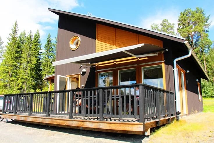 En timrad stuga vid Skellefteå camping med en veranda i trä, omgiven av grönska och trädgårdsytor.