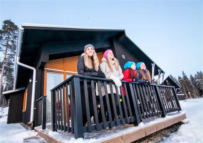 En vinterbild visar Skellefteå camping med snöklädda stugor och omgivning. Log cabiner står omgivna av gnistrande snö och frost under en klar himmel, vilket ger en känsla av avkoppling och vintersportmöjligheter.