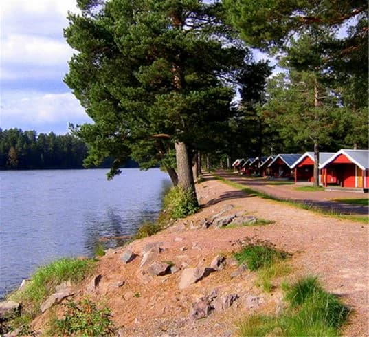 Bild av älvdalens camping som visar en vacker sjö med klart vatten och omgivande gröna landskap. Stranden vid sjöns kant ger en naturskön vy av området.