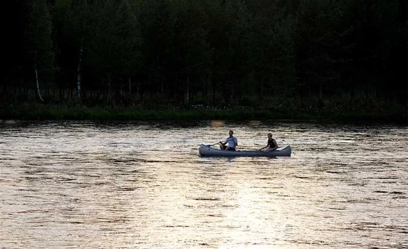 En naturskön campingplats vid en vattenväg med flera båtar vid stranden, omgiven av vild natur, vilket erbjuder möjligheter till friluftsliv och båtliv.