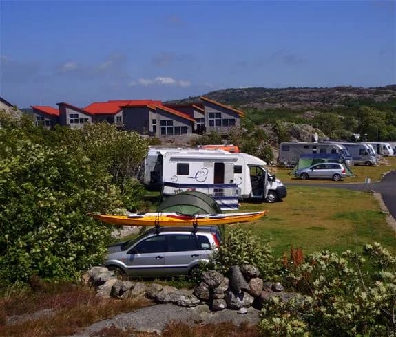 En skåpbil parkerad på en grusväg vid Hav & Logi Skärhamn, omgiven av grönska och med skymtar av havet i bakgrunden.