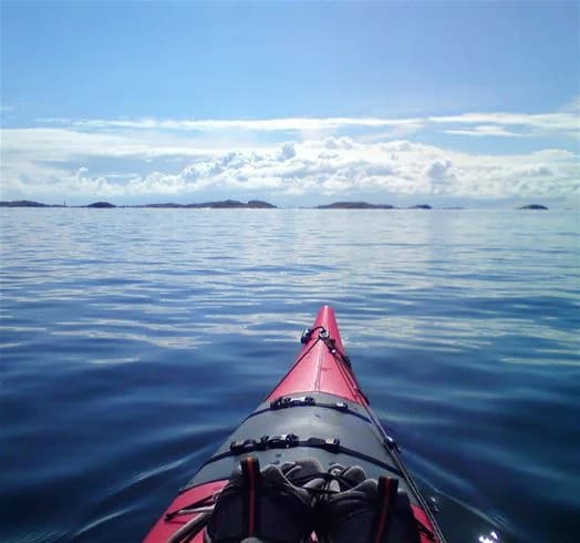 En grupp kajakpaddlare färdas genom stilla vatten i en kustnära miljö vid Skärhamn, omgivna av hav och låga öar.