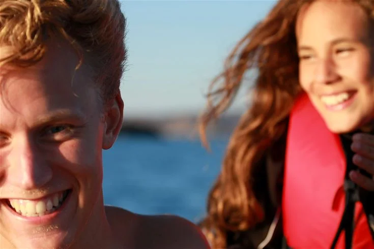 En leende person med brunt hår njuter av en solig dag vid hav & logi Skärhamn, skapar en känsla av semester och avkoppling.