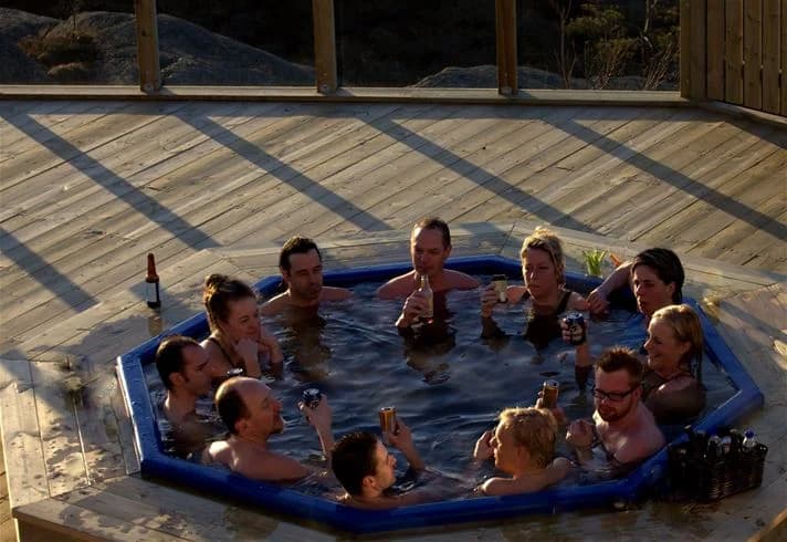 En solig dag vid en pool på Hav & Logi Skärhamn. Flera personer kopplar av och njuter av semesterstämningen, några badar i poolen medan andra solar vid kanten.