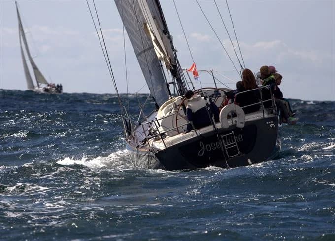 En segelbåt i havet med upphissade segel under en klar himmel nära Skärhamn, med glittrande vatten i bakgrunden.