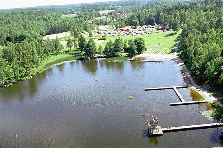 En naturskön vy vid Malmköpings Bad & Camping som visar ett glittrande vatten omgivet av lummiga träd och grönska.