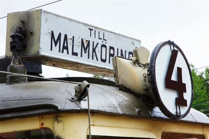 En bild av ett tåg som passerar nära Malmköpings Bad & Camping, med fokus på loket och dess vindruta. I bakgrunden syns delar av campingområdet.