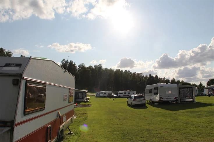 Bild av en campingplats i Malmköping med husvagnar uppställda på en gräsmatta. Omgivningen består av gröna ängar och träd, vilket skapar en naturskön och avkopplande miljö för besökare.