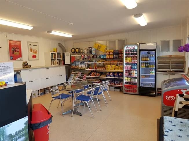 En interiörbild av en butik eller reception på Vivstavarvstjärns camping. Bilden visar golv, hyllor fyllda med diverse varor, möbler och ljus takbelysning, vilket skapar en inbjudande atmosfär för besökare.