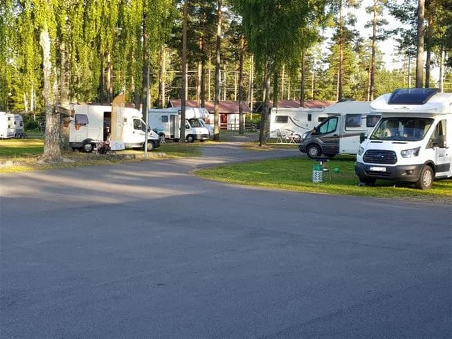 En uppställningsplats på Vivstavarvstjärns camping med flera husbilar och husvagnar parkerade på en grusplan. Träd syns i bakgrunden.