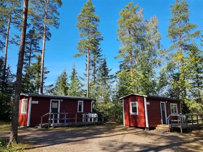 En bild av Vivstavarvstjärns Camping med en mysig timmerstuga omgiven av grönskande träd och en rymlig gård.
